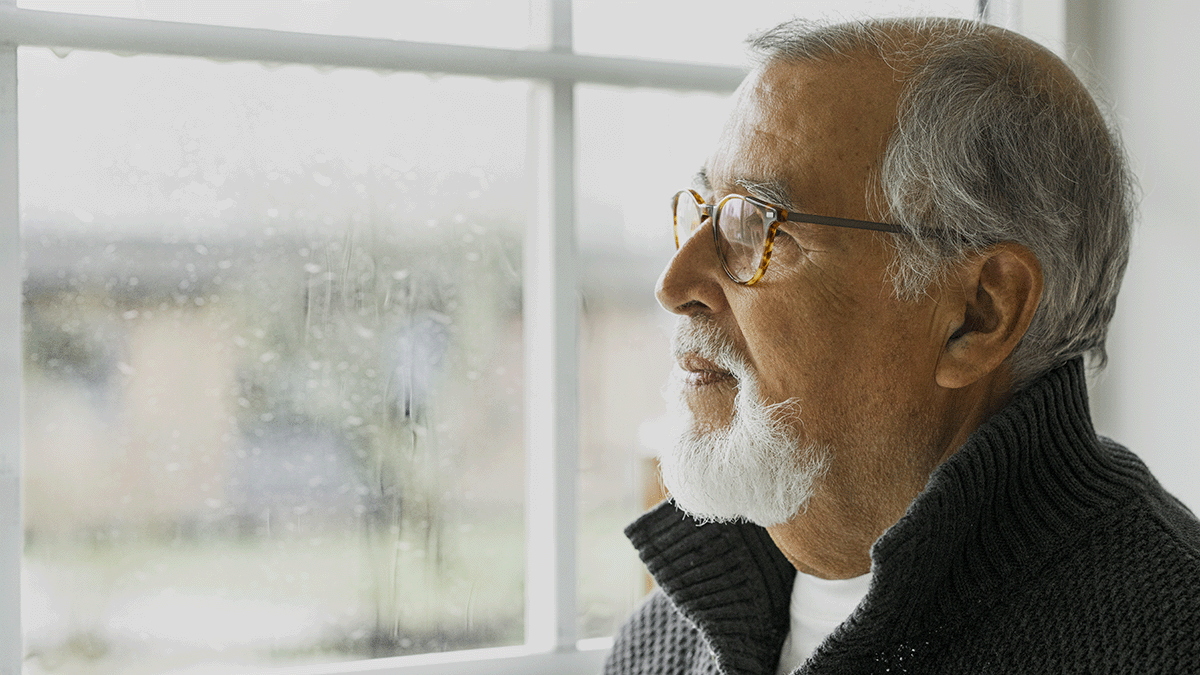 A sad elderly gentleman looking out through a window. Photo. 