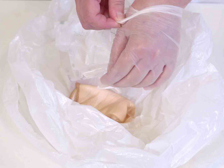 A photo of two hands placing a wound dressing and disposable gloves in a plastic bag. 