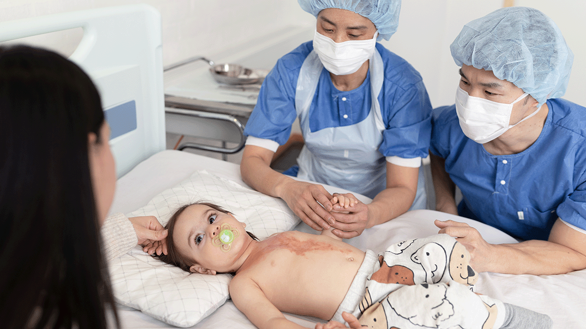 A photo of a toddler with severe burns in a hospital bed. A mother and two doctors are tending to the child. 