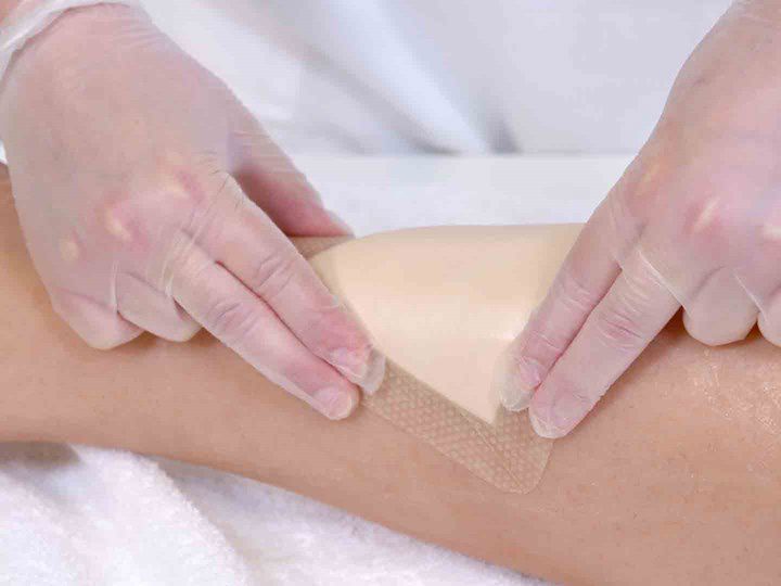 A photo of two hands holding down a wound dressing over a wound.