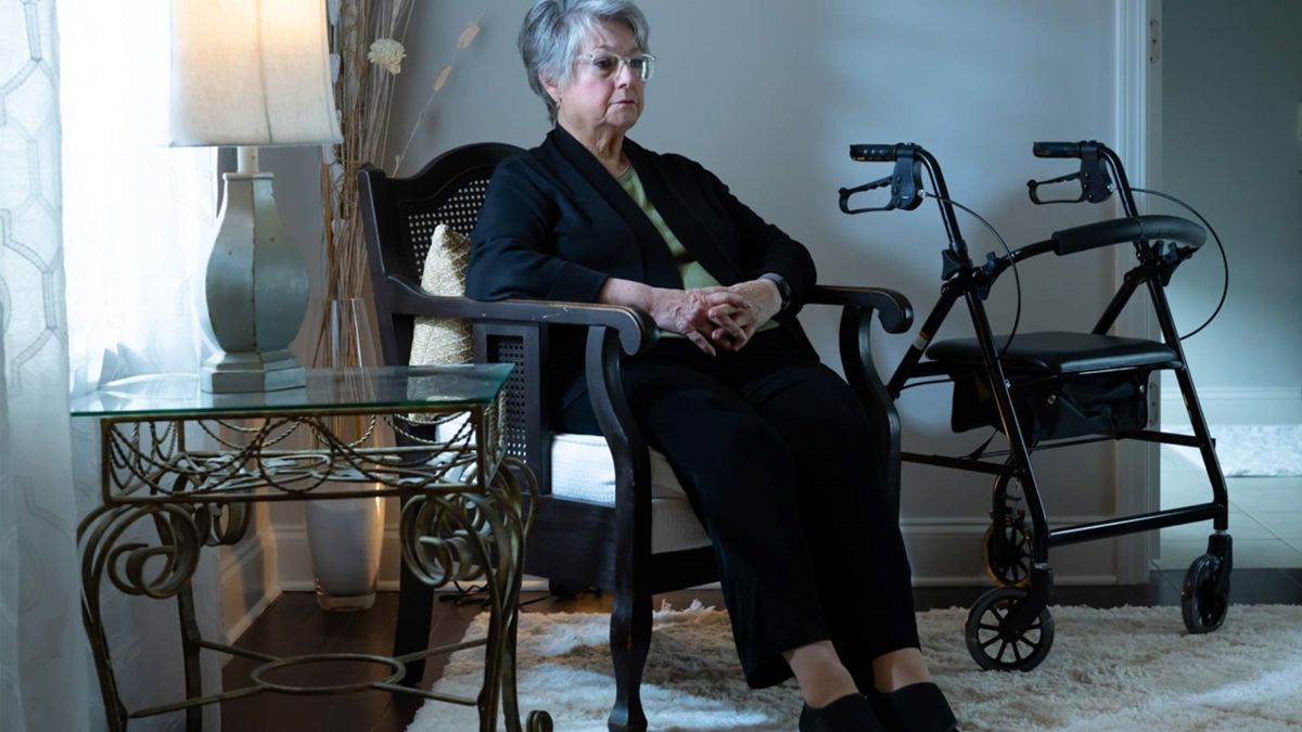 A photo of a sad elderly woman sitting alone next to her walker. 