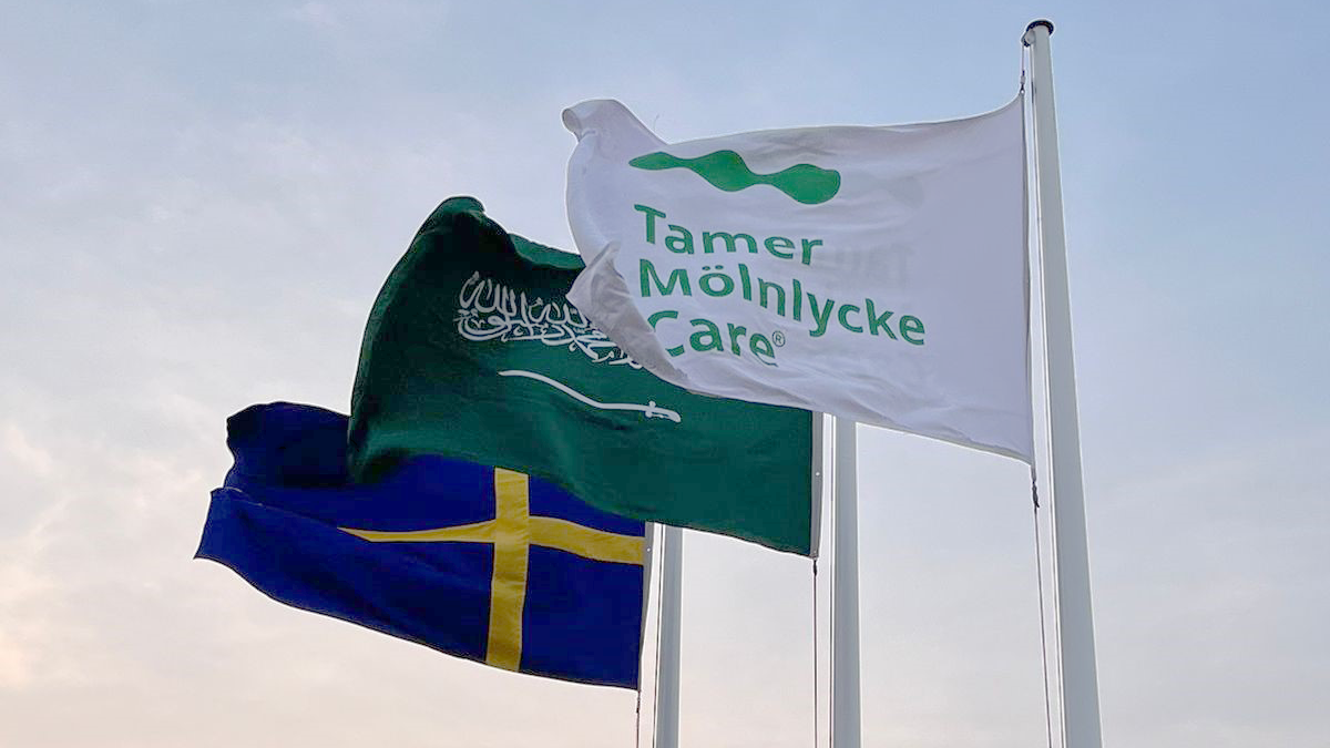 Three flags in a sunset; the Swedish flag, the Saudi Arabian flag and the Tamer Mölnlycke flag. Photo.