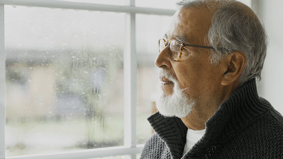 An elderly gentleman looking sadly on the rain outside his window. Photo. 
