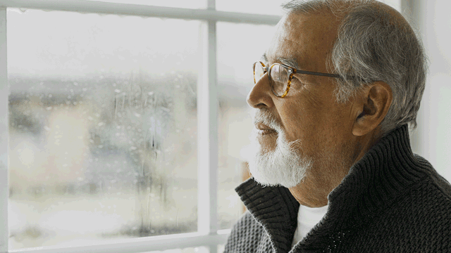 An elderly gentleman looking sadly on the rain outside his window. Photo. 
