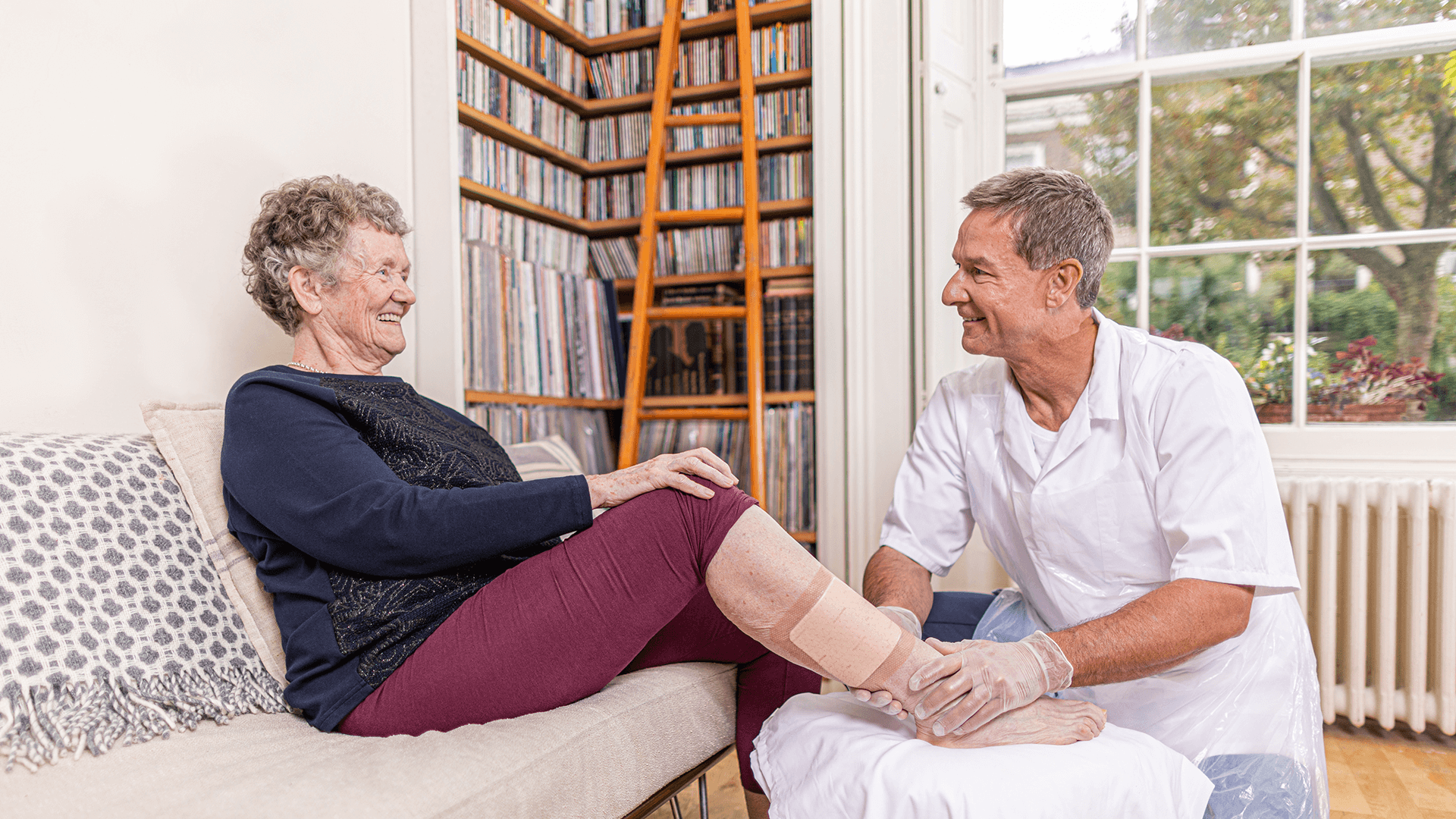 A photo of a male nurse helping an elderly lady with a leg ulcer. 