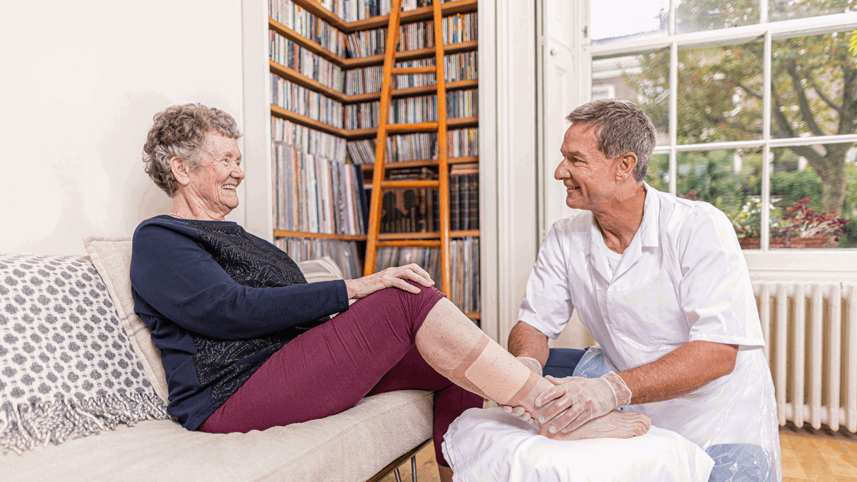 A photo of a male nurse helping an elderly lady with a leg ulcer. 