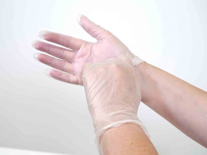 A photo of hands putting on disposable gloves. 