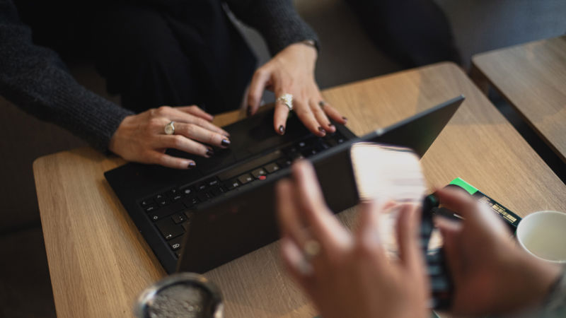 Close-up of people using a laptop and smartphone at a table, representing collaborative work and responsible decision-making