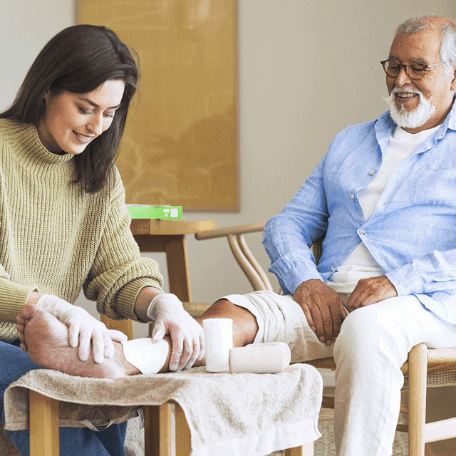 A photo of a nurse tending to a patient's leg in a home environment.