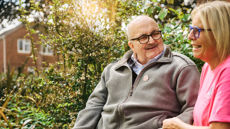 A patient and caregiver healthcare professional sitting outside and smiling